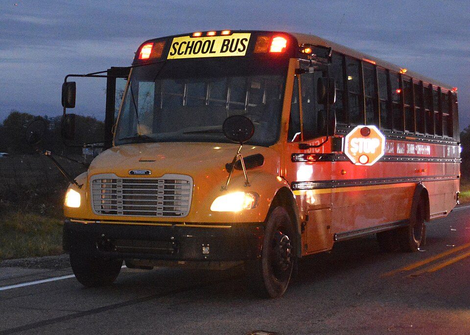 The side of a yellow school bus with a red octagonal stop arm swung out
